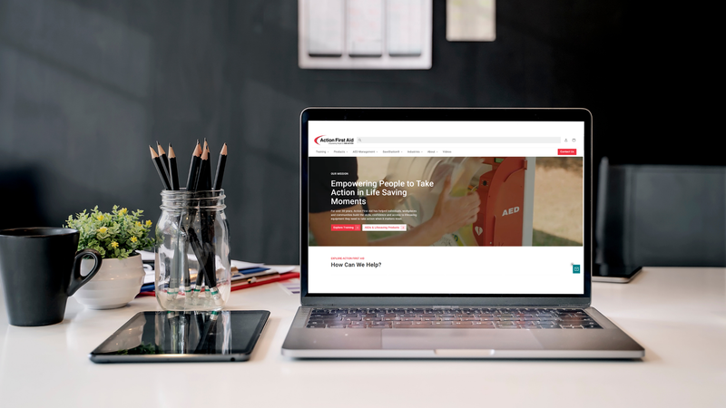 Action First Aid Website on Open Laptop on desk with pencils plant and coffee mug